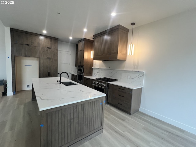 kitchen with premium range hood, decorative light fixtures, sink, high end stainless steel range oven, and a center island with sink