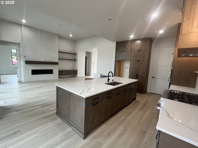 kitchen with sink, a large fireplace, light stone counters, light hardwood / wood-style floors, and a spacious island