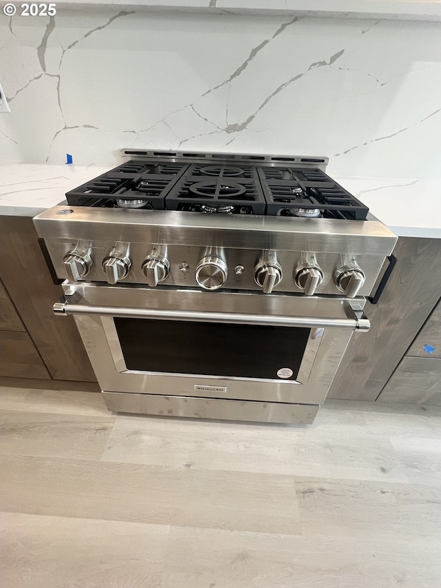 details with high end stainless steel range oven, light wood-type flooring, backsplash, and light stone counters