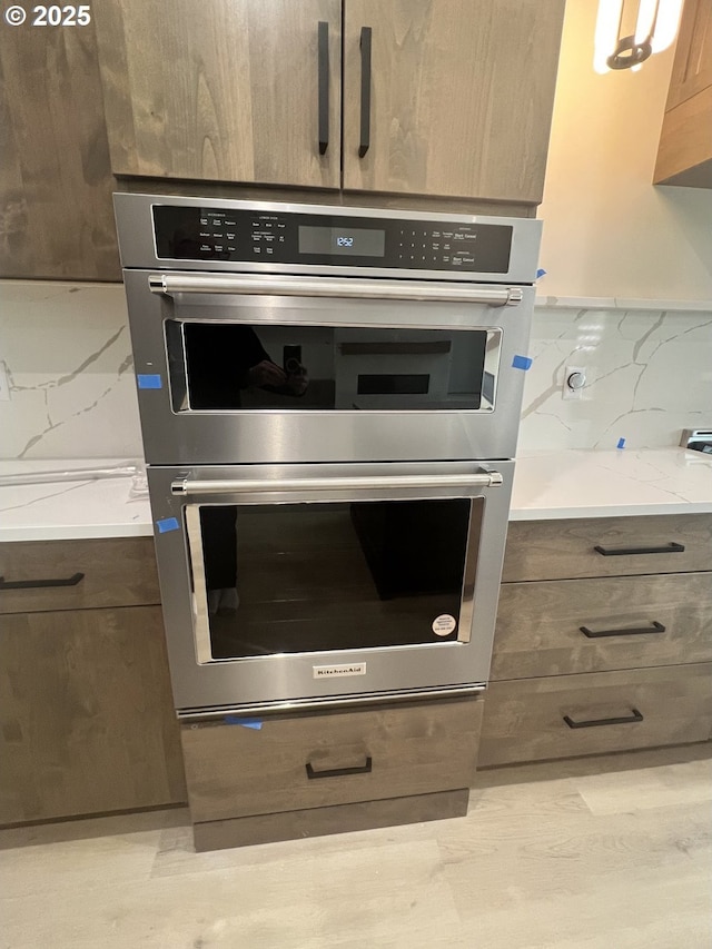 room details featuring light stone counters, double oven, and decorative backsplash