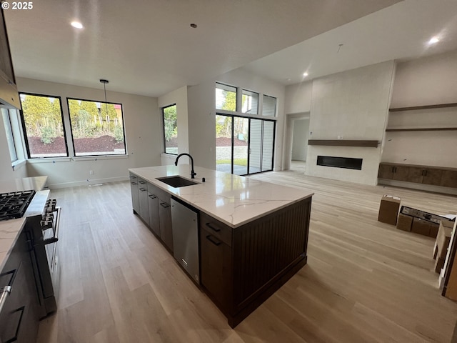 kitchen with sink, dishwasher, dark brown cabinetry, a fireplace, and an island with sink