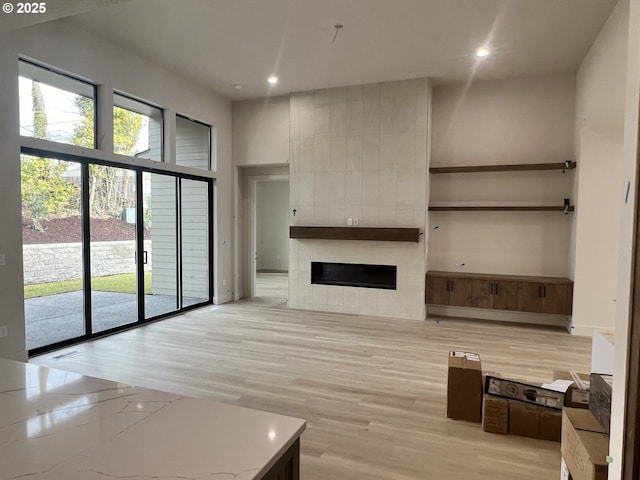 unfurnished living room featuring a tile fireplace, a towering ceiling, and light hardwood / wood-style floors