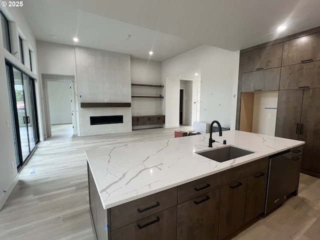 kitchen featuring sink, light stone counters, light wood-type flooring, an island with sink, and a tile fireplace