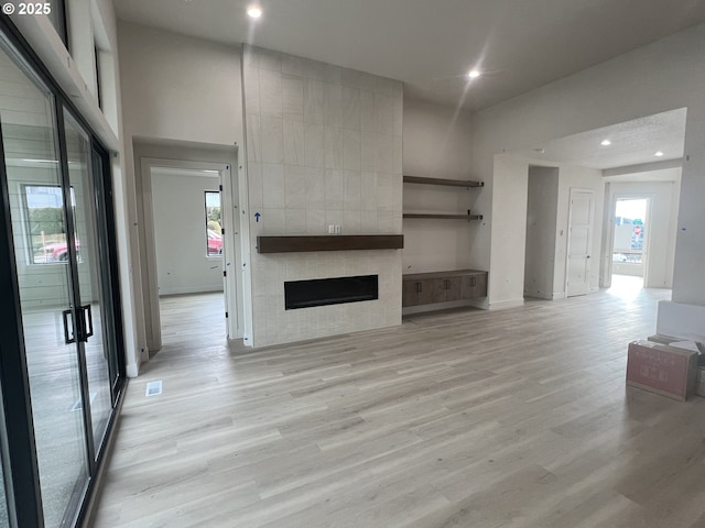 unfurnished living room with a tiled fireplace, a towering ceiling, and light hardwood / wood-style flooring