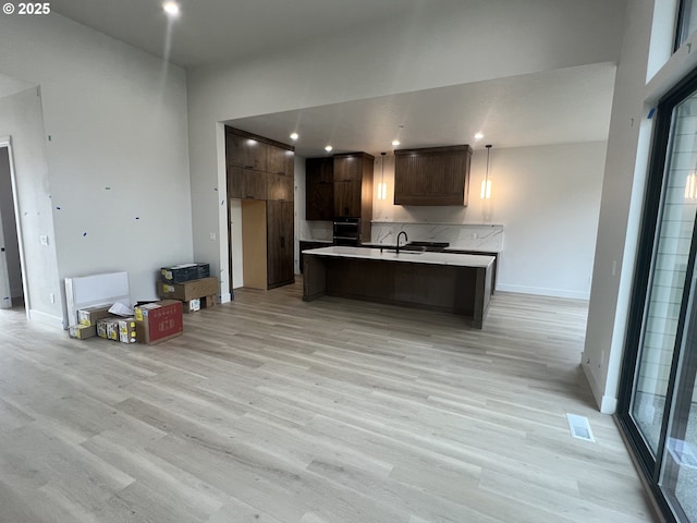 kitchen featuring pendant lighting, black oven, dark brown cabinets, a center island with sink, and light hardwood / wood-style flooring