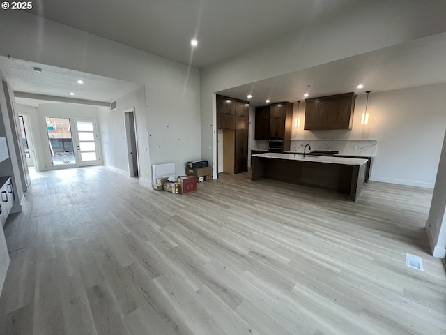 kitchen featuring dark brown cabinets, a kitchen island with sink, black oven, and light wood-type flooring