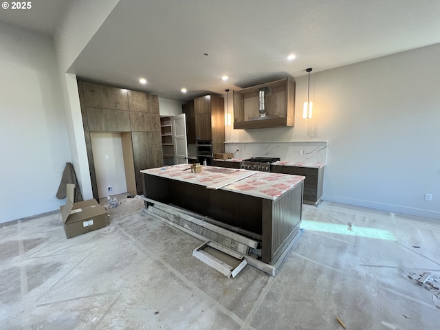 kitchen with pendant lighting, black double oven, stainless steel range, wall chimney range hood, and a center island with sink