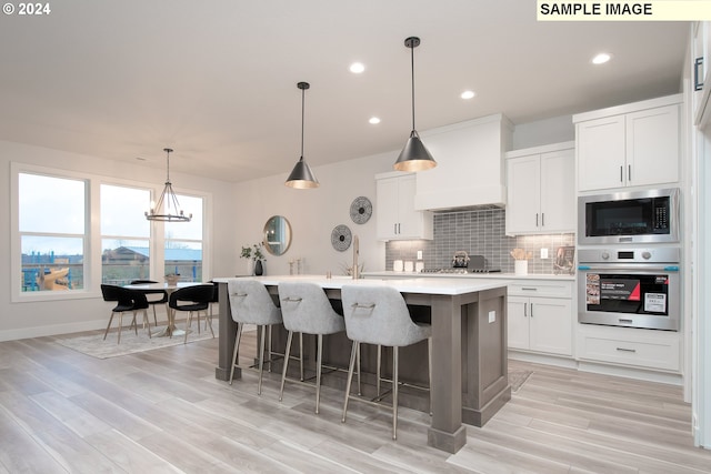 kitchen with stainless steel oven, custom exhaust hood, built in microwave, white cabinets, and a center island with sink