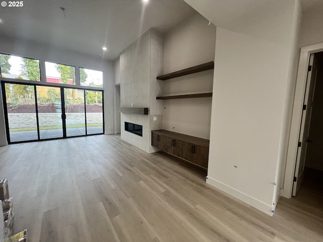 unfurnished living room with a fireplace, light hardwood / wood-style flooring, and a high ceiling