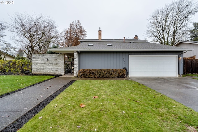 view of front of house with fence, roof with shingles, a front yard, a garage, and driveway