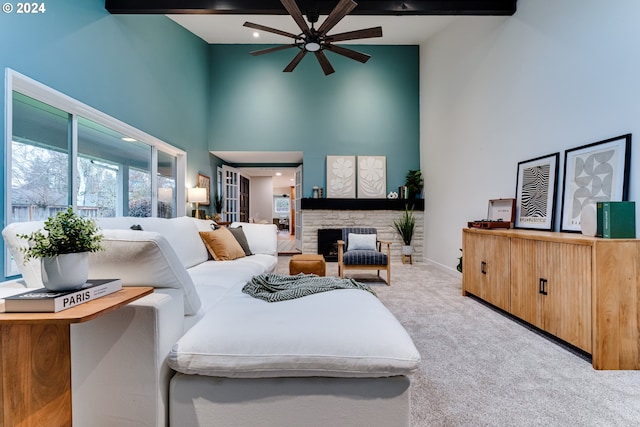 carpeted living area featuring ceiling fan, baseboards, beam ceiling, a stone fireplace, and a towering ceiling