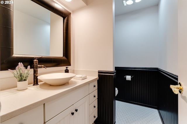 half bathroom featuring a wainscoted wall, toilet, and vanity