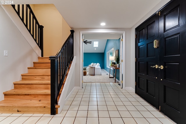 entrance foyer with light tile patterned floors, baseboards, light colored carpet, and stairs