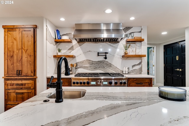 kitchen featuring open shelves, a sink, tasteful backsplash, wall chimney range hood, and light stone countertops