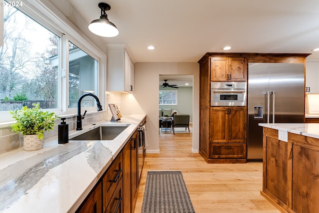 kitchen with light stone counters, light wood finished floors, stainless steel appliances, decorative backsplash, and a sink