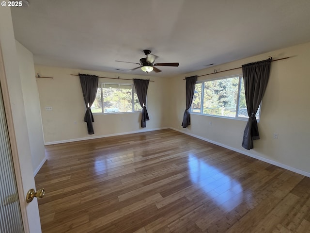 empty room featuring a ceiling fan, visible vents, baseboards, and wood finished floors