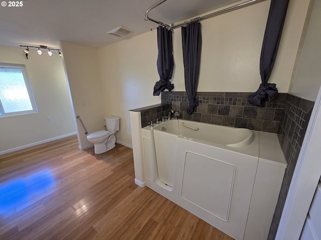 full bath with a garden tub, toilet, wood finished floors, visible vents, and baseboards