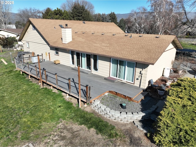 exterior space featuring a shingled roof, a lawn, a chimney, and a wooden deck