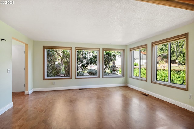 spare room with visible vents, a textured ceiling, baseboards, and wood finished floors