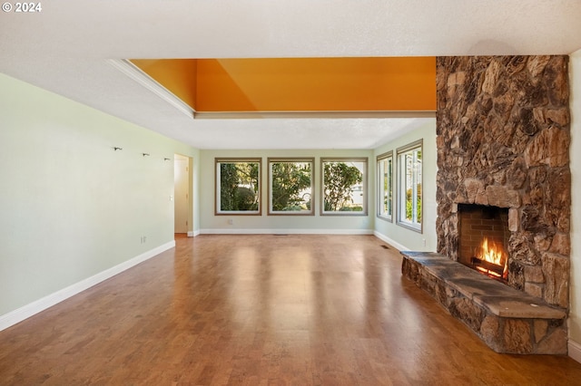 unfurnished living room with hardwood / wood-style floors, a stone fireplace, and a tray ceiling