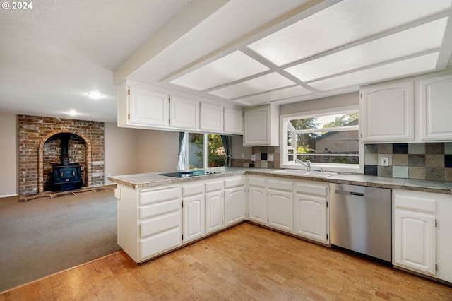 kitchen featuring a wood stove, white cabinetry, sink, stainless steel dishwasher, and kitchen peninsula