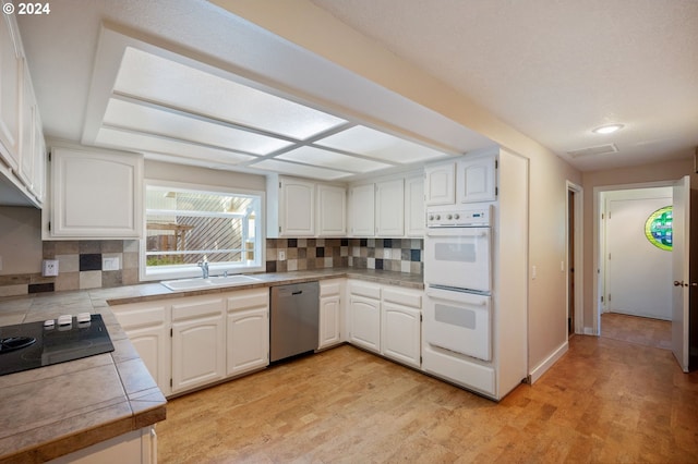 kitchen with dishwasher, white double oven, white cabinets, and sink