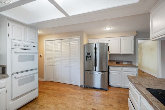 kitchen with tile counters, white cabinets, white double oven, black electric stovetop, and stainless steel refrigerator with ice dispenser