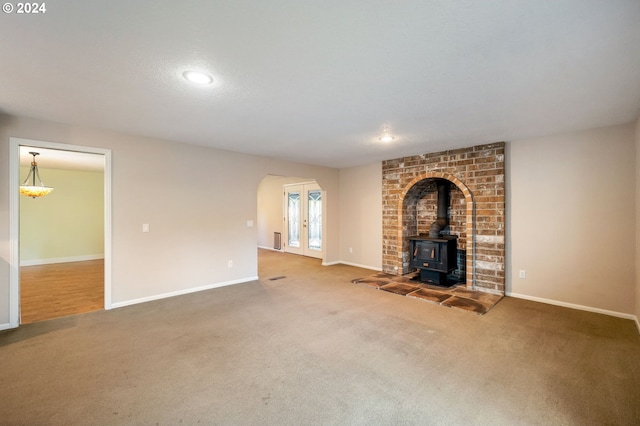 unfurnished living room featuring carpet floors, french doors, baseboards, and a wood stove