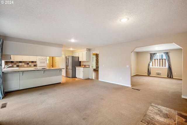 kitchen with a peninsula, white cabinetry, open floor plan, light countertops, and stainless steel refrigerator with ice dispenser