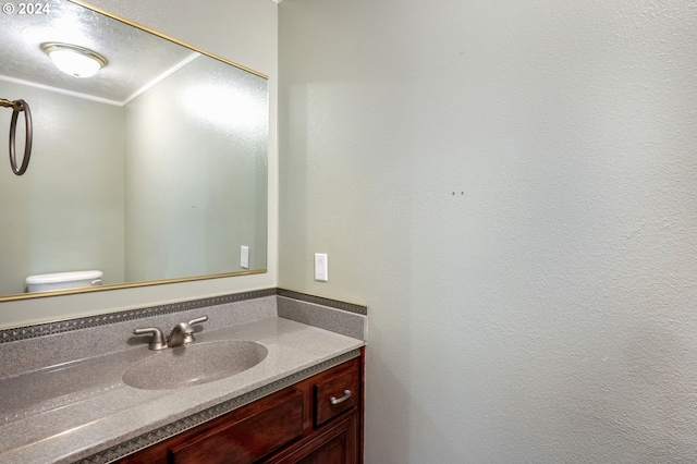 bathroom with a textured ceiling, vanity, toilet, and crown molding