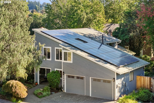 view of side of home with an attached garage, driveway, fence, and solar panels