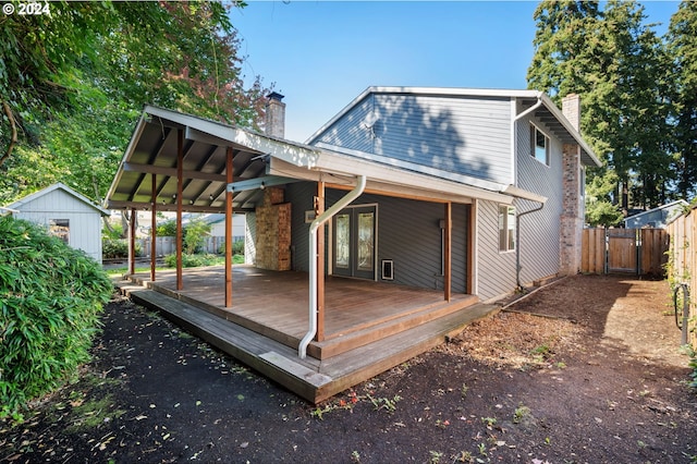 rear view of property featuring a chimney, an outdoor structure, fence, and a wooden deck