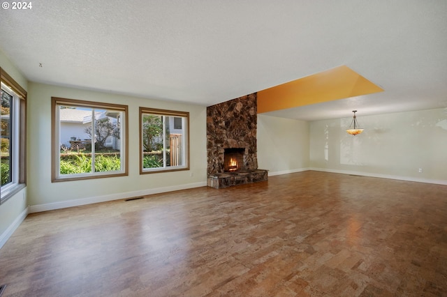 unfurnished living room with plenty of natural light, a stone fireplace, and a textured ceiling