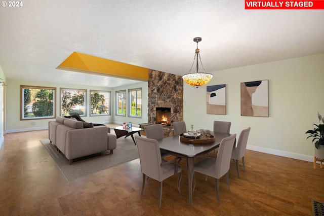 dining room with a stone fireplace, baseboards, and a textured ceiling