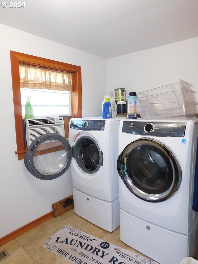 clothes washing area featuring light tile patterned floors, an AC wall unit, and washer and clothes dryer