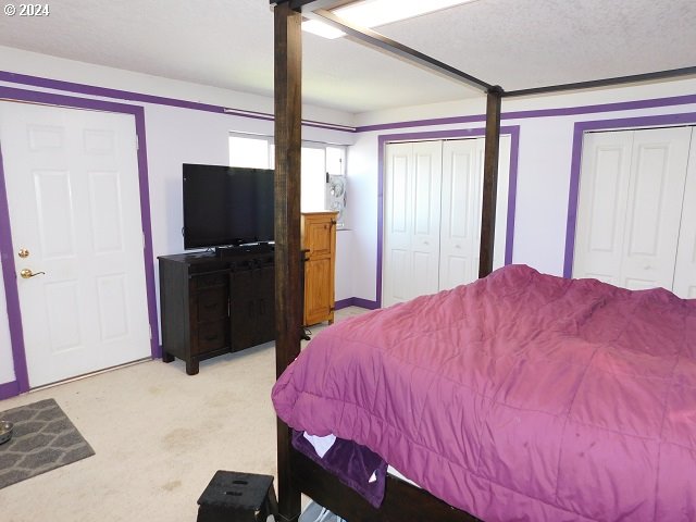 bedroom featuring a textured ceiling, light colored carpet, and two closets