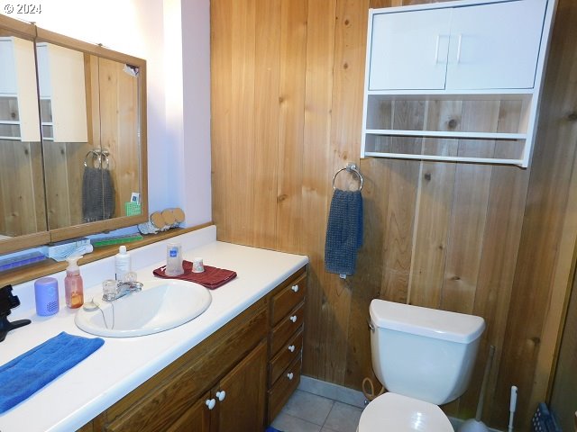 bathroom featuring wooden walls, tile patterned flooring, vanity, and toilet