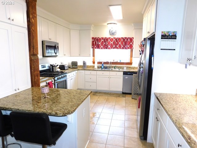 kitchen featuring a breakfast bar, stainless steel appliances, sink, light tile patterned floors, and white cabinets