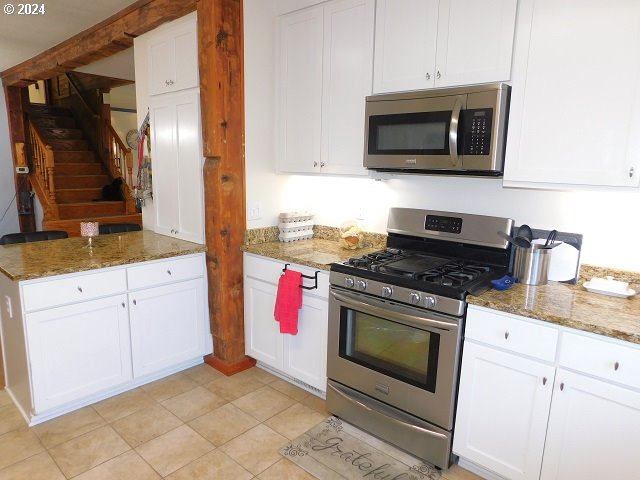 kitchen with white cabinets, light tile patterned floors, appliances with stainless steel finishes, and dark stone counters