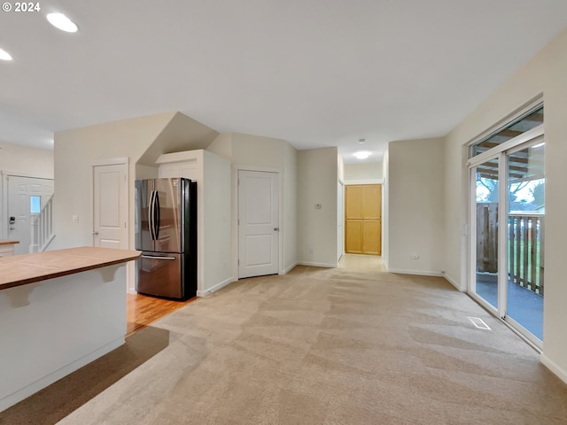 kitchen featuring wood counters, stainless steel fridge, light colored carpet, and white cabinetry