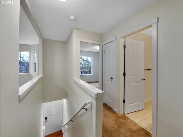 corridor with a textured ceiling, light colored carpet, and a healthy amount of sunlight