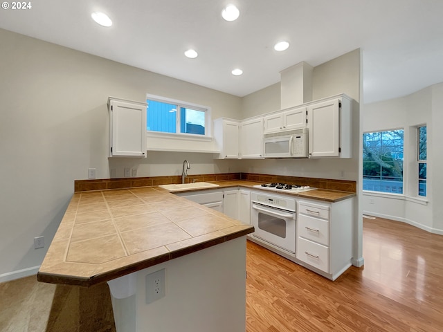 kitchen featuring kitchen peninsula, tile countertops, white cabinets, and white appliances