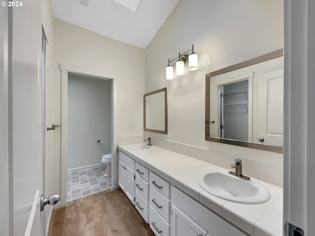 bathroom with vaulted ceiling with skylight, vanity, and toilet