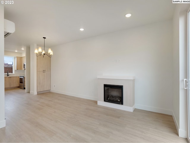 unfurnished living room with an inviting chandelier, light hardwood / wood-style flooring, and a wall unit AC