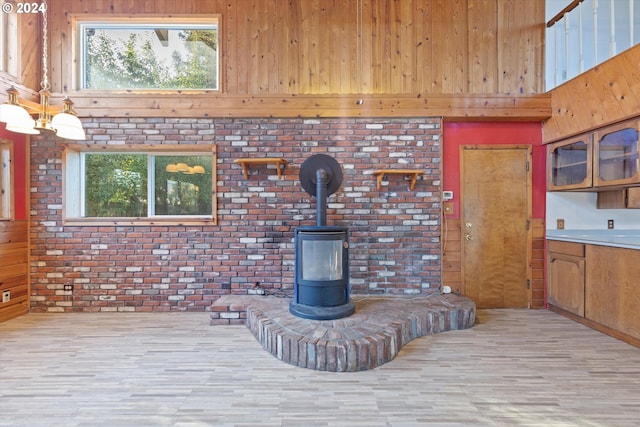 living room featuring light wood-type flooring, brick wall, a high ceiling, a wood stove, and wood walls