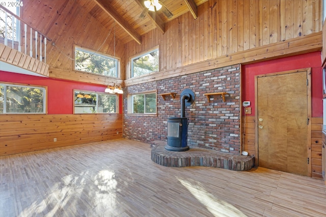 unfurnished living room featuring hardwood / wood-style flooring, beam ceiling, a wood stove, and wooden walls