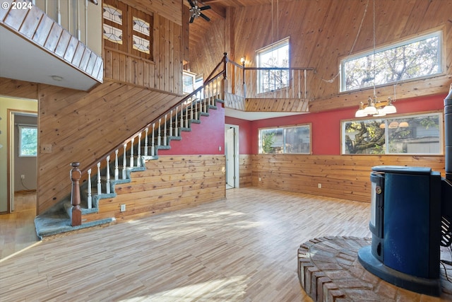 unfurnished living room with plenty of natural light, a wood stove, a high ceiling, and wooden walls