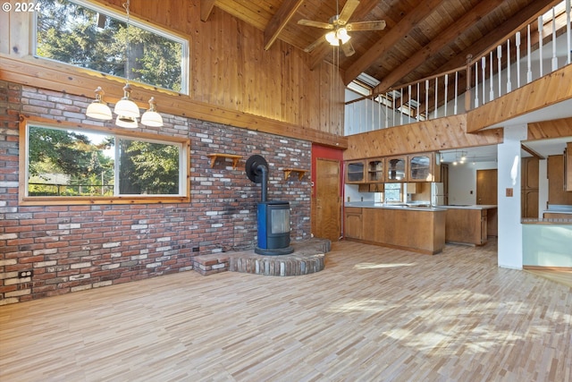 unfurnished living room featuring beam ceiling, high vaulted ceiling, a wood stove, and plenty of natural light