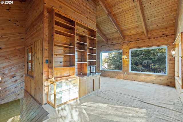 unfurnished living room with beam ceiling, wooden walls, high vaulted ceiling, and light carpet