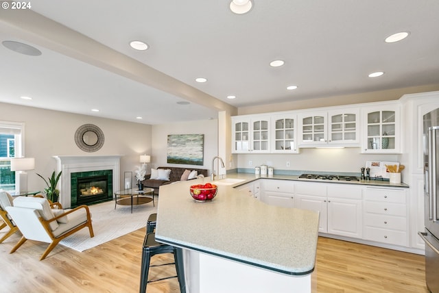 kitchen featuring white cabinets, glass insert cabinets, open floor plan, a peninsula, and a sink